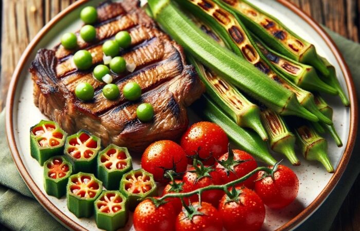 A white ceramic plate featuring grilled meat, green ladies finger vegetables (okra), and red cherry tomatoes. The grilled meat has golden-brown grill